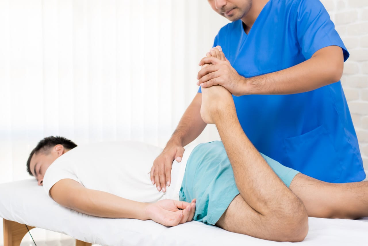Physiotherapist stretching leg of male patient on the bed in hospital - physical therapy concept